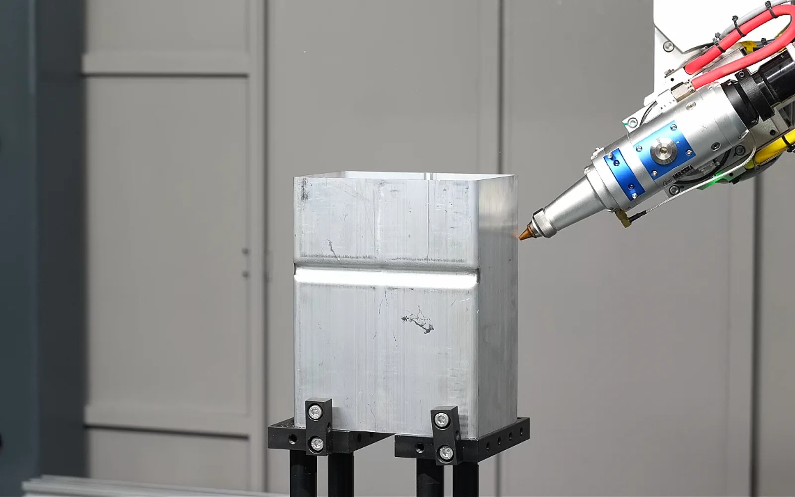 Five-axis laser cutting head approaching a metal part at an angle